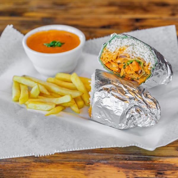CurryGrill's chicken tikka burrito, fries, and orange dipping sauce on a wooden table.