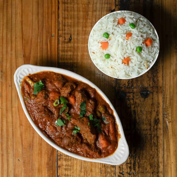 CurryGrill's Indian curry with meat and vegetables, served with a side of rice and peas.