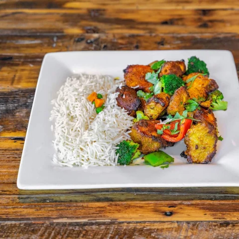 Indian dish with basmati rice, spiced chicken or paneer, broccoli, and bell peppers on a white plate.