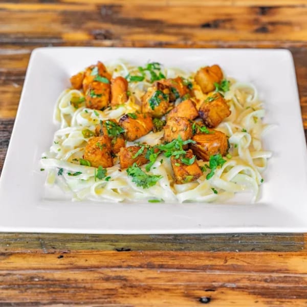 Indian chicken tikka masala with fettuccine pasta and cilantro on a white plate.