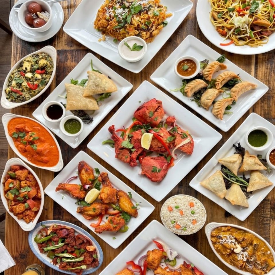 Overhead view of a wooden table laden with various Indian dishes in white serving plates.