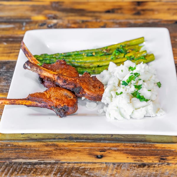 Grilled lamb chops with asparagus and mashed potatoes on a white rectangular plate.