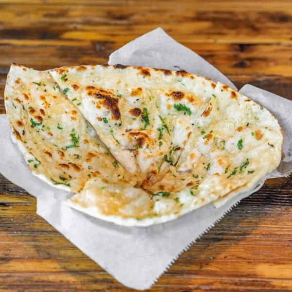 Garlic naan, a traditional Indian flatbread, served in a paper-lined basket on a wooden table.