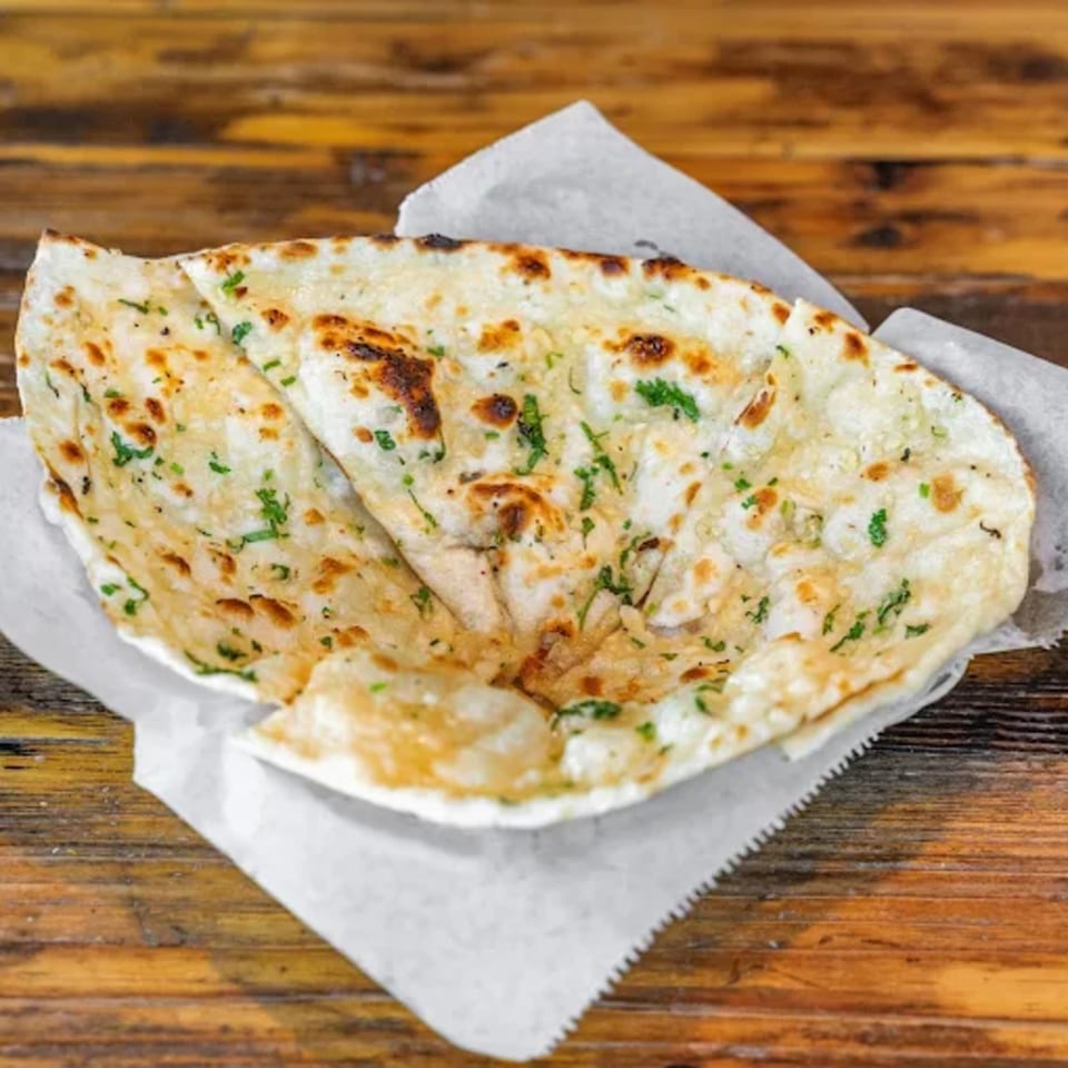 Garlic naan, a traditional Indian flatbread, served in a paper-lined basket on a wooden table.